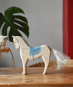 Ostheimer wooden white horse with small blue saddle placed on a wooden surface.