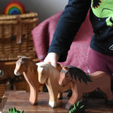 Three large Ostheimer wooden horse toy figures lined up on a wooden stool, child standing on the background.