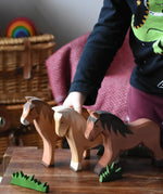 Three large Ostheimer wooden horse toy figures lined up on a wooden stool, child standing on the background.