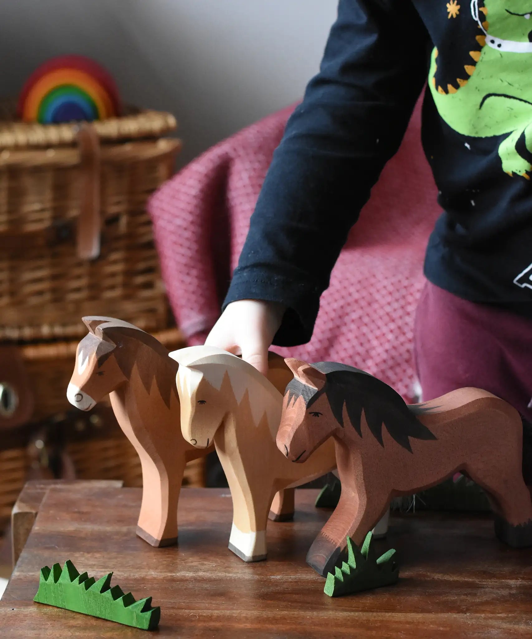 Three large Ostheimer wooden horse toy figures lined up on a wooden stool, child standing on the background.