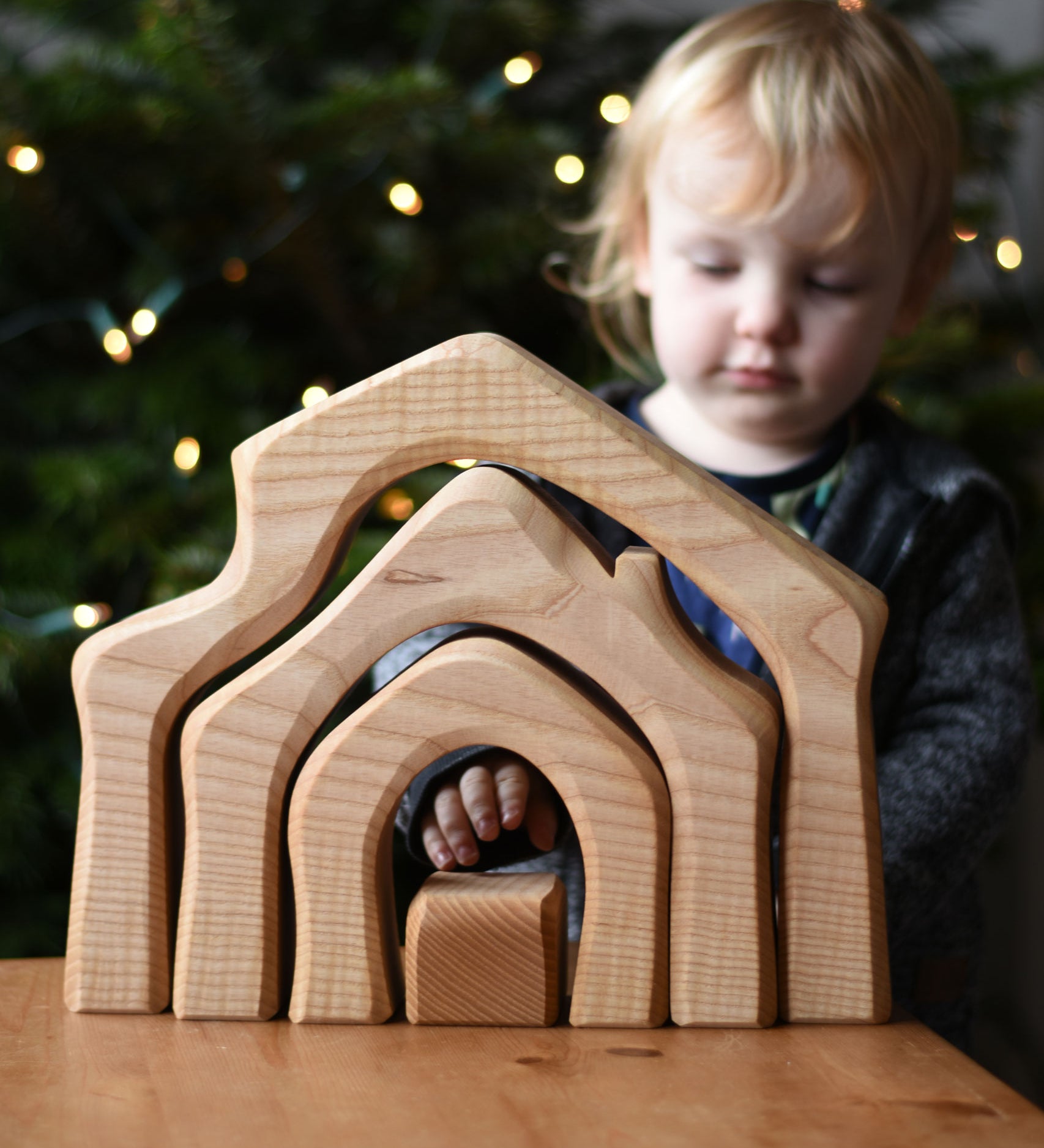A child standing behind the Ostheimer 4 Piece Wooden House Parts that has been placed on a wooden table. Ostheimer have a range of wooden toy figures and scenery pieces that are perfect for small world play available at Babipur. 
