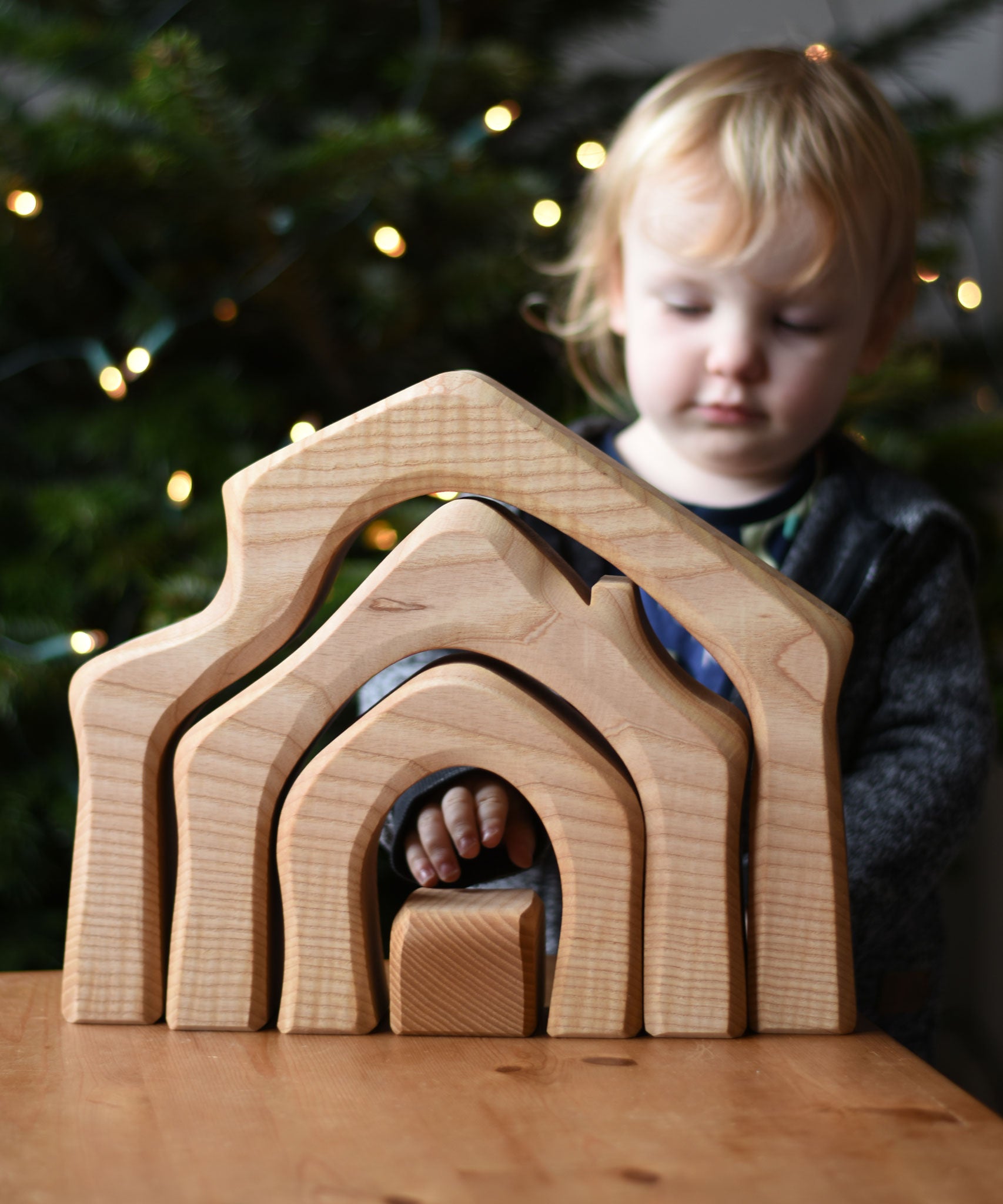 A child standing behind the Ostheimer 4 Piece Wooden House Parts that has been placed on a wooden table. Ostheimer have a range of wooden toy figures and scenery pieces that are perfect for small world play available at Babipur. 