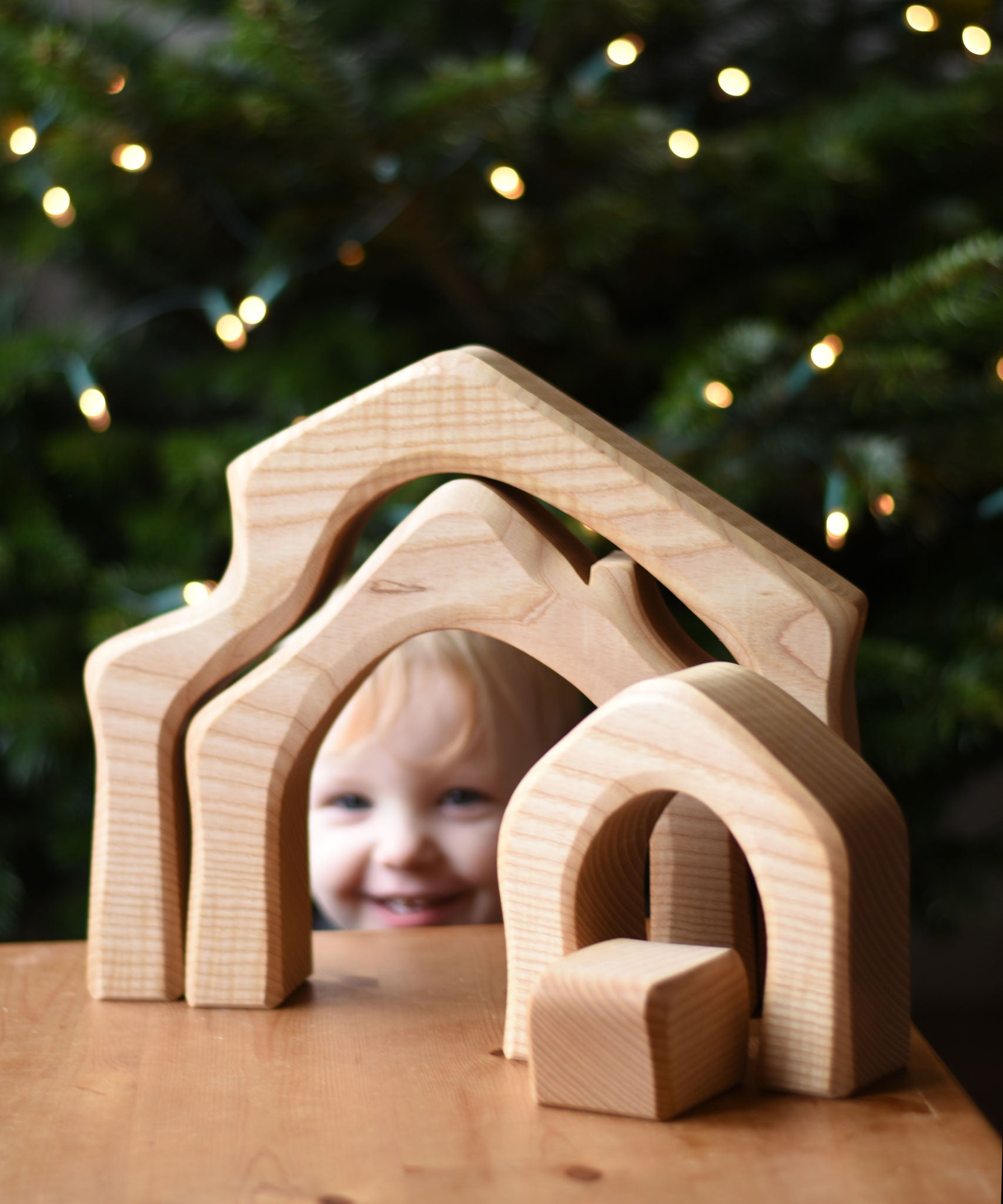 A child behind the Ostheimer 4 Piece Wooden House Parts that has been placed on a wooden table, peeping through the house shaped piece. Ostheimer have a range of wooden toy figures and scenery pieces that are perfect for small world play available at Babipur. 