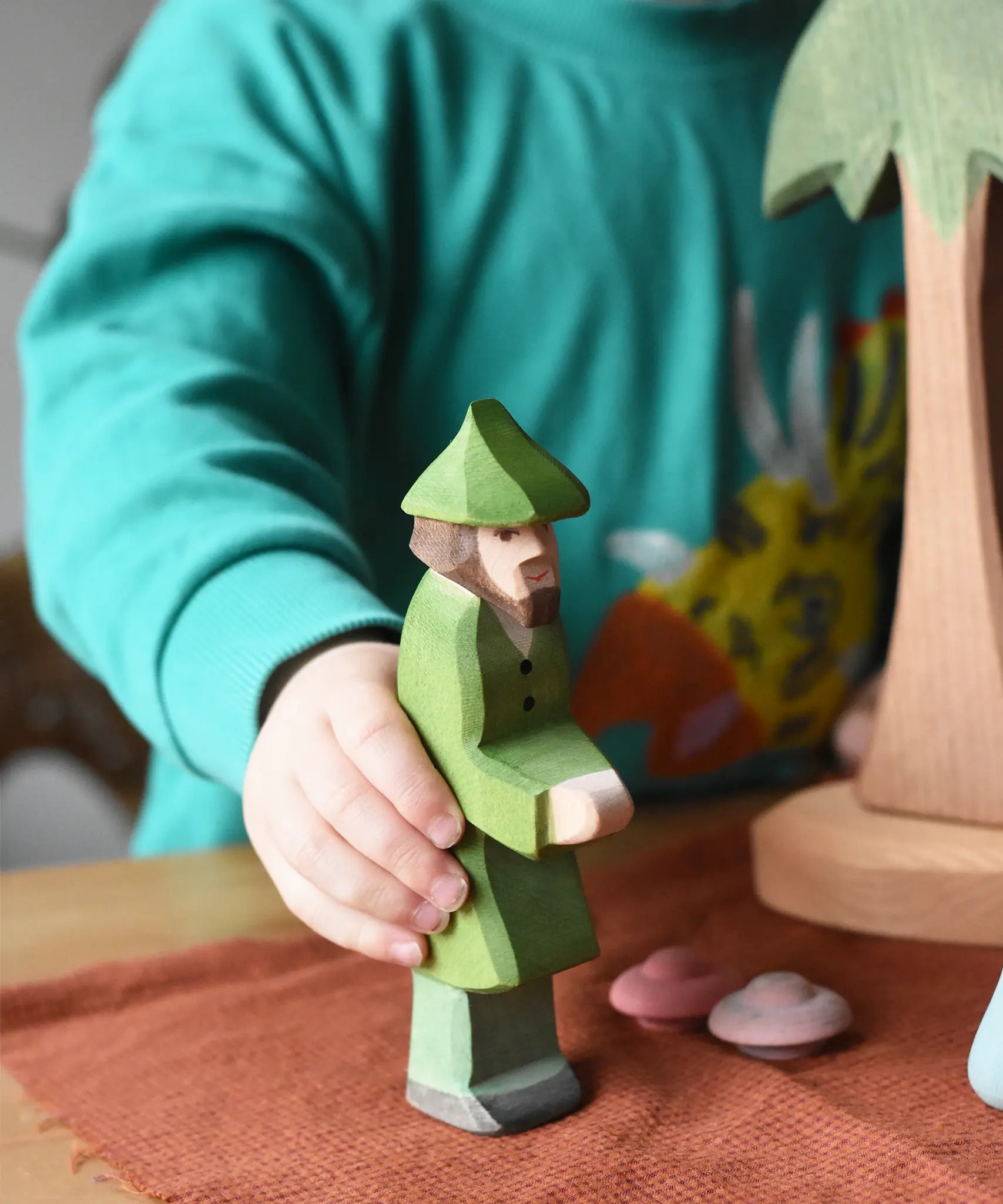 Ostheimer hunter wooden toy figure in a child's hand in a small world play scene. 