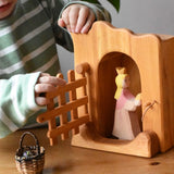 Ostheimer jailhouse wooden toy in a small world play scene with a princess for frog king placed inside, a child opening the front trellised gate.