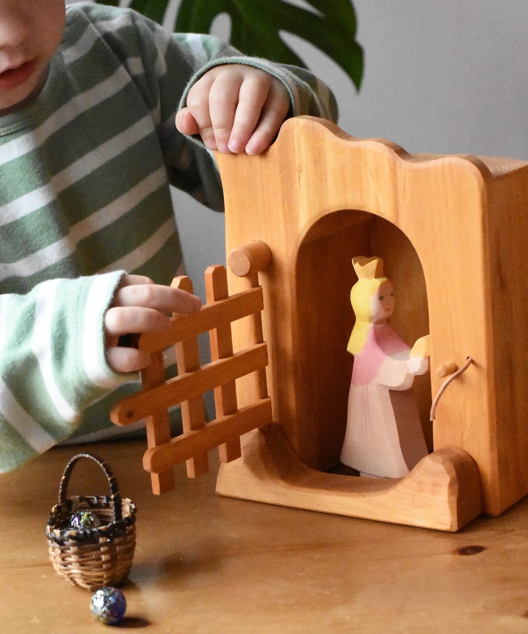 Ostheimer jailhouse wooden toy in a small world play scene with a princess for frog king placed inside, a child opening the front trellised gate.