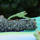 Ostheimer jumping frog handmade wooden toy figure placed on a lichen covered branch. 