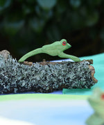 Ostheimer jumping frog handmade wooden toy figure placed on a lichen covered branch. 