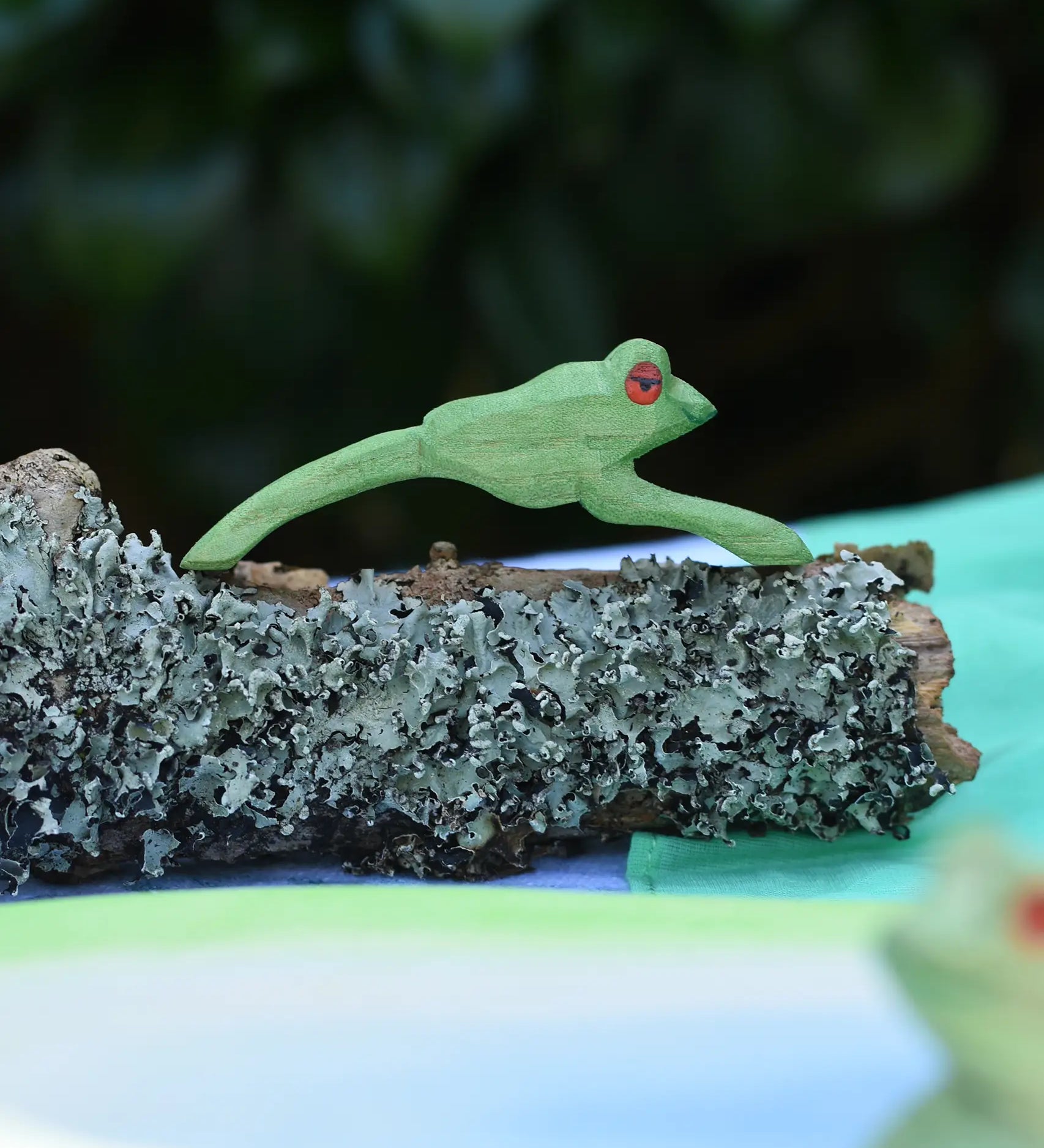 Ostheimer jumping frog handmade wooden toy figure placed on a lichen covered branch. 