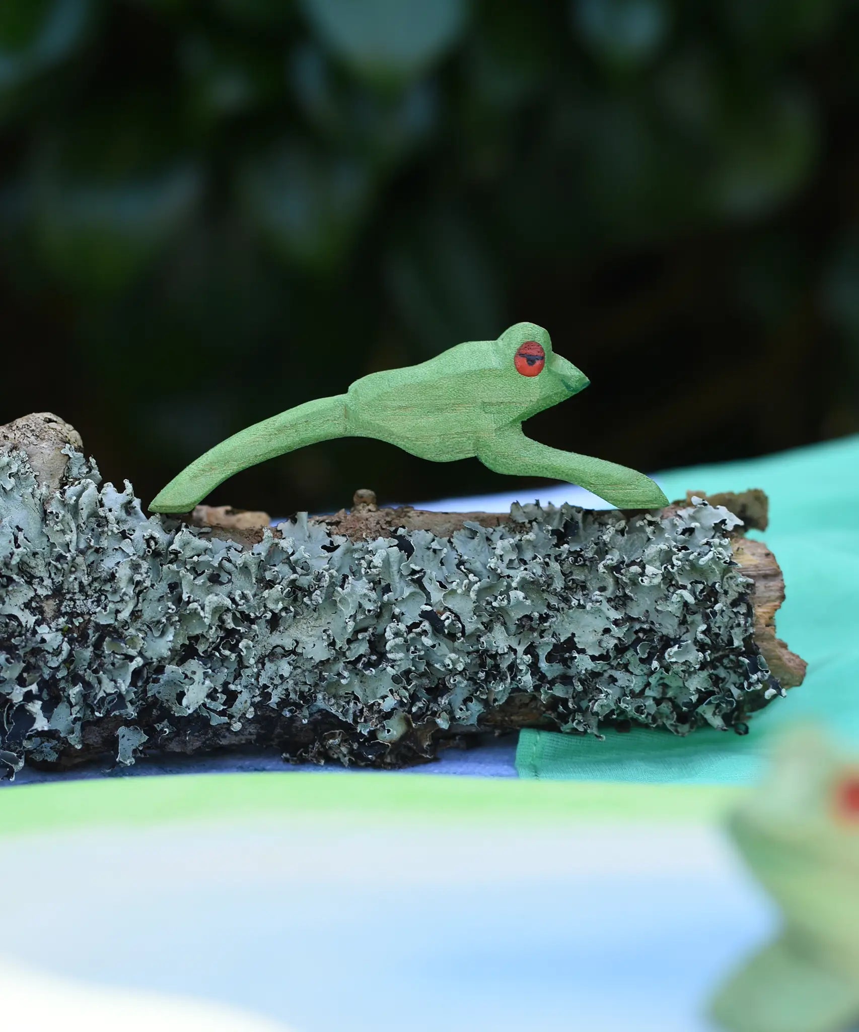 Ostheimer jumping frog handmade wooden toy figure placed on a lichen covered branch. 