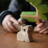 An Ostheimer koala placed on a wooden surface, a child can be seen in the bachground playing with a Ostheimer eucalyptus tree. These wooden figures are part of a wide range of expertly hand crafted wooden toys here at Babipur. 