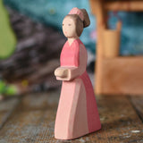 An Ostheimer hand made wooden Lady-In-Waiting toy figure placed on a wooden surface in a small world play scene. Other wooden toys including an Ostheimer water well can be seen in the background. These wooden figures are part of a wide range of expertly hand crafted wooden toys here at Babipur. 