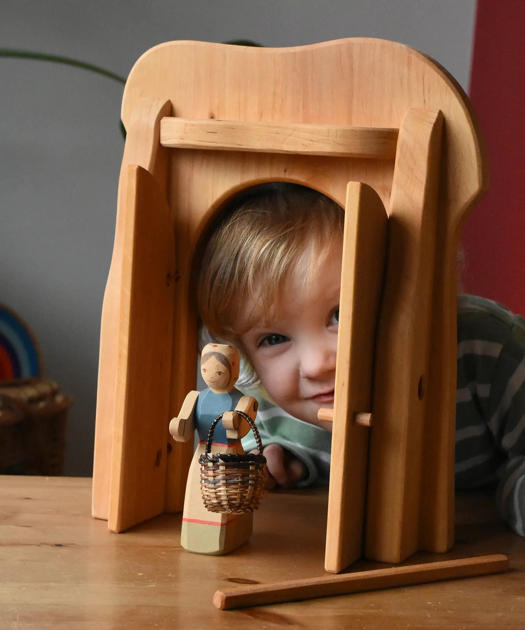 Ostheimer castle gate with a female farmer figure holding  a small Kraul basket in front. Child peering through the open doors.
