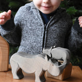 The large Ostheimer rhino wooden toy figure placed on a wooden surface. A child can be seen looking on excitedly in the background. These wooden figures are part of a wide range of expertly hand crafted wooden toys here at Babipur.