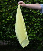 Ostheimer lemon yellow decorative play scarf held in a child's hand outdoors.