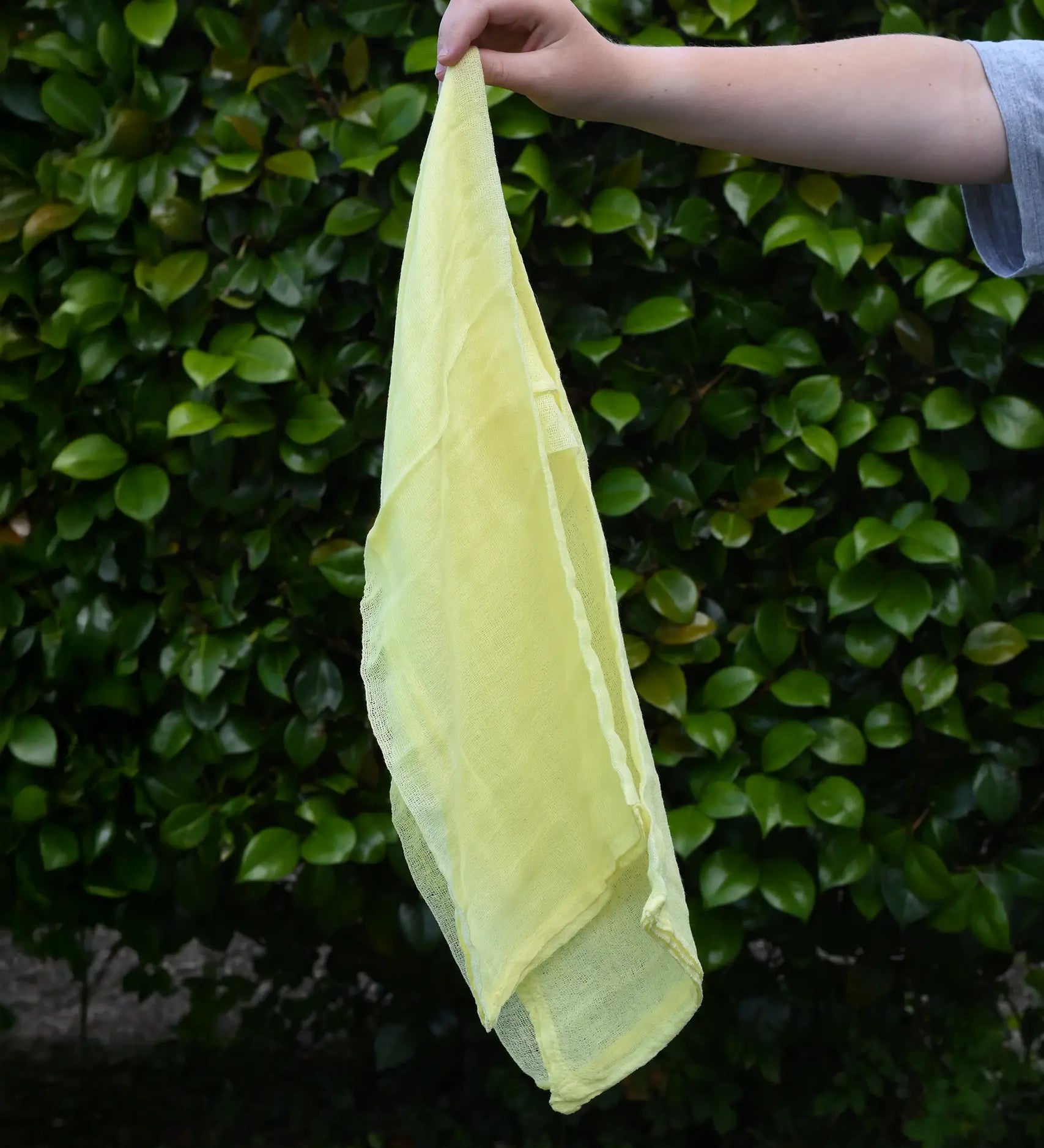 Ostheimer lemon yellow decorative play scarf held in a child's hand outdoors.