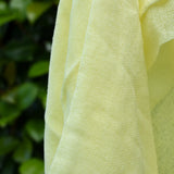 Close up of the weave on the Ostheimer lemon yellow decorative play scarf held in a child's hand outdoors.