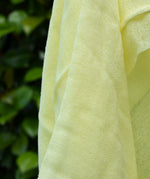 Close up of the weave on the Ostheimer lemon yellow decorative play scarf held in a child's hand outdoors.
