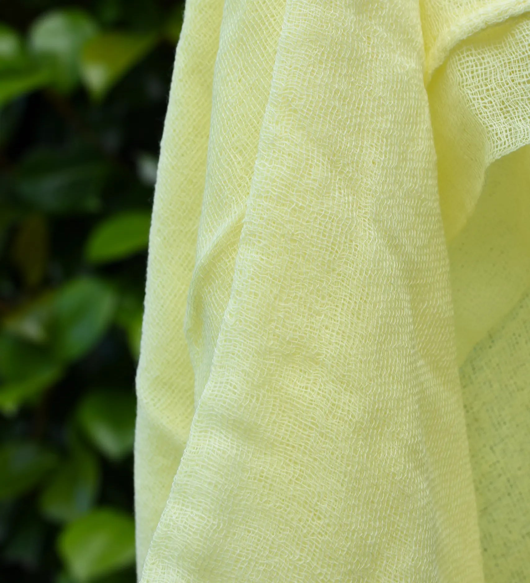 Close up of the weave on the Ostheimer lemon yellow decorative play scarf held in a child's hand outdoors.