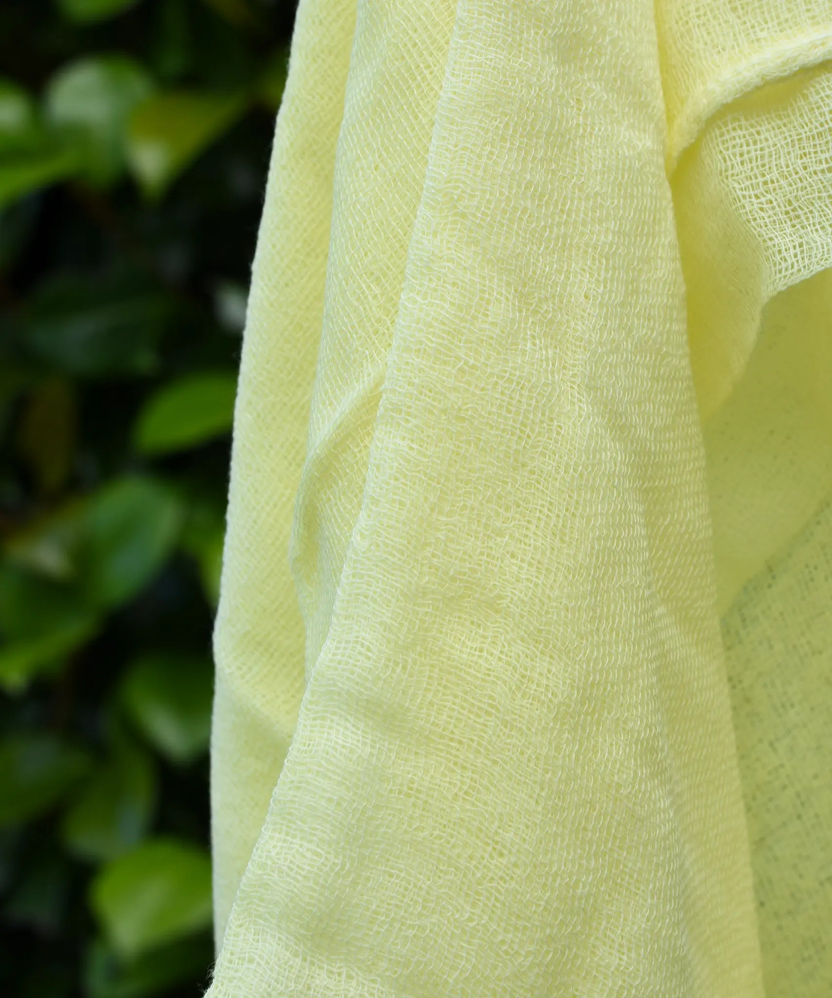 Close up of the weave on the Ostheimer lemon yellow decorative play scarf held in a child's hand outdoors.
