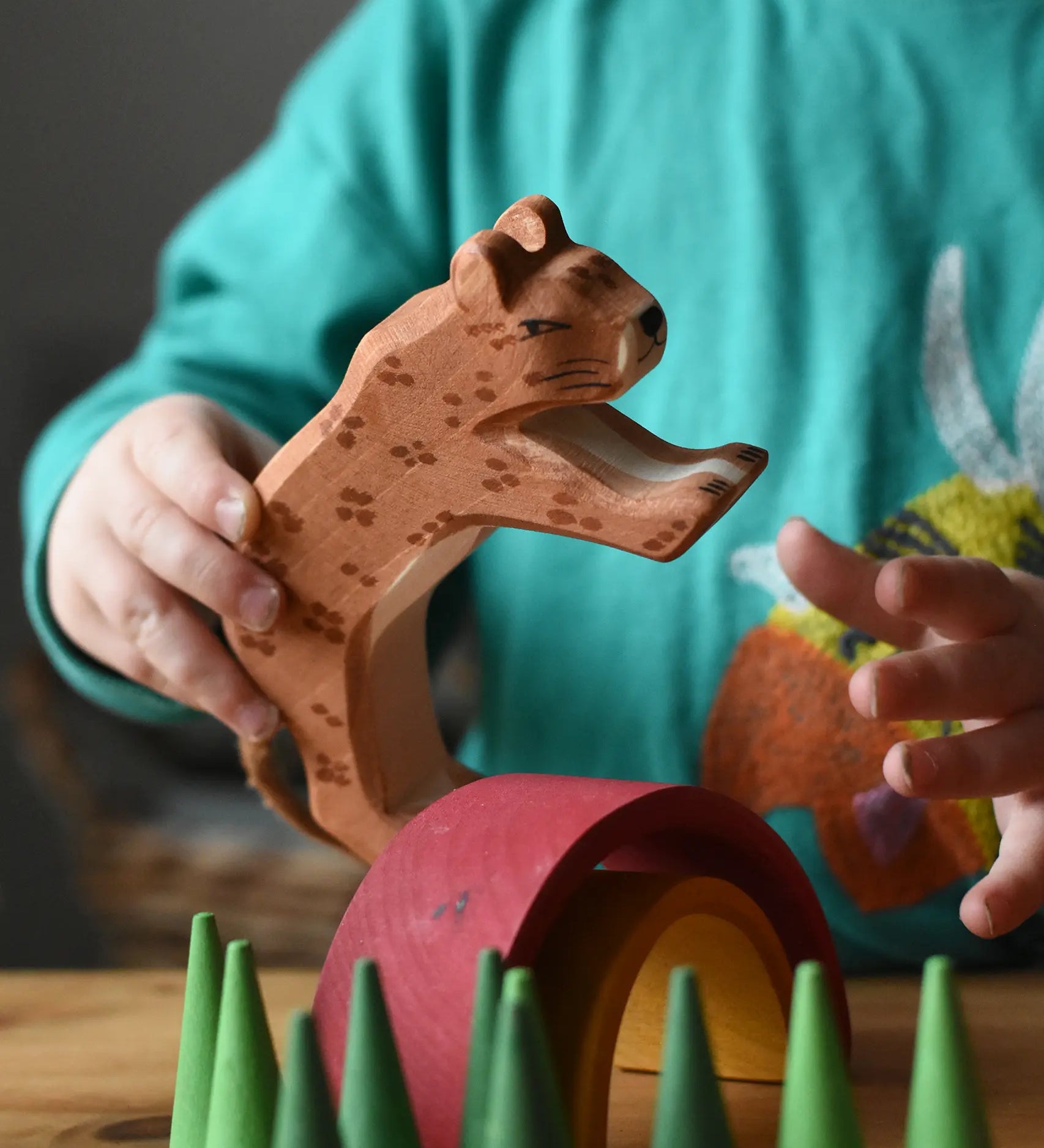 Ostheimer leopard in a child's hand resting on a mini Grimm's rainbow surrounded with green cone Grapat mandala pieces. 