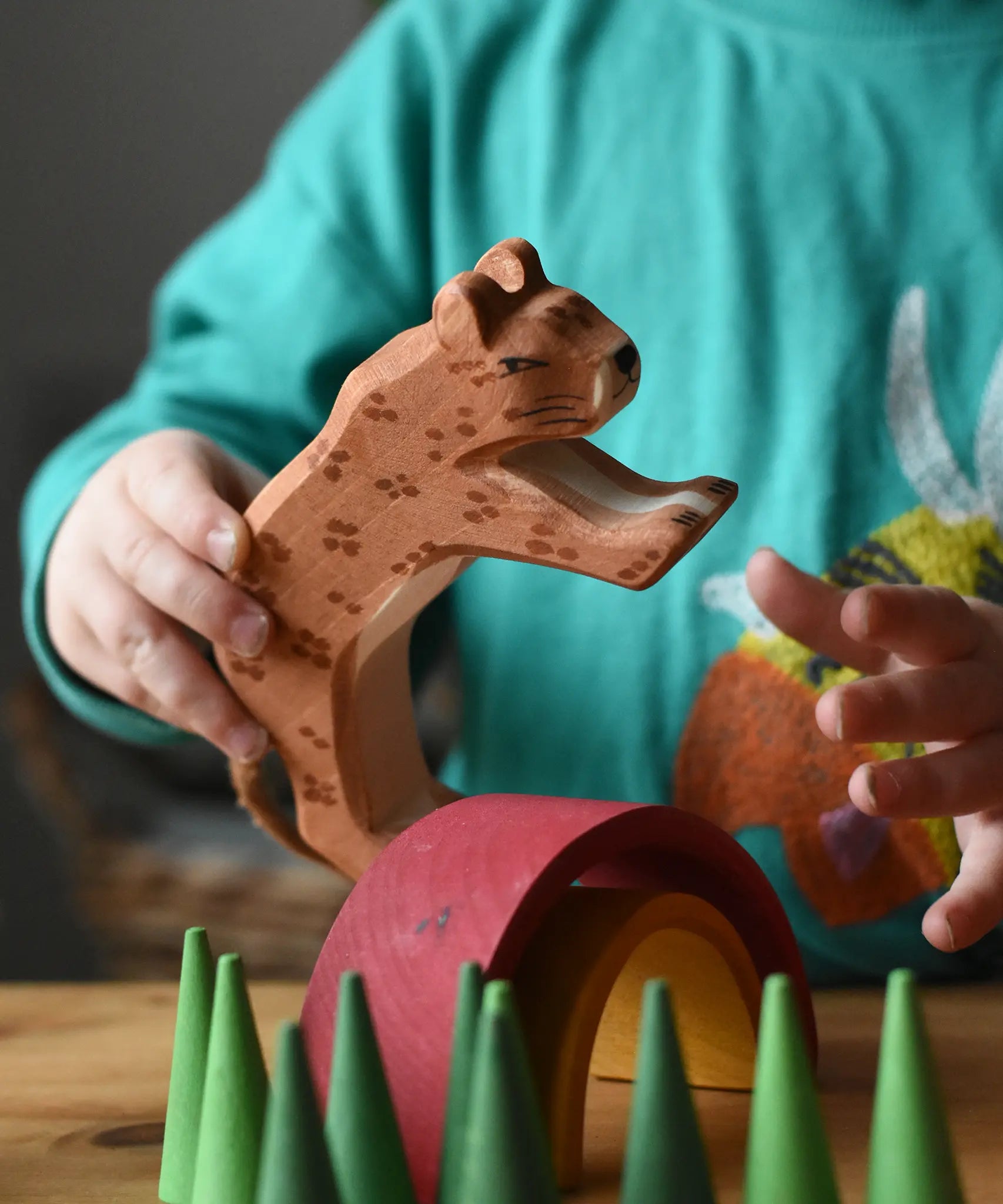 Ostheimer leopard in a child's hand resting on a mini Grimm's rainbow surrounded with green cone Grapat mandala pieces. 