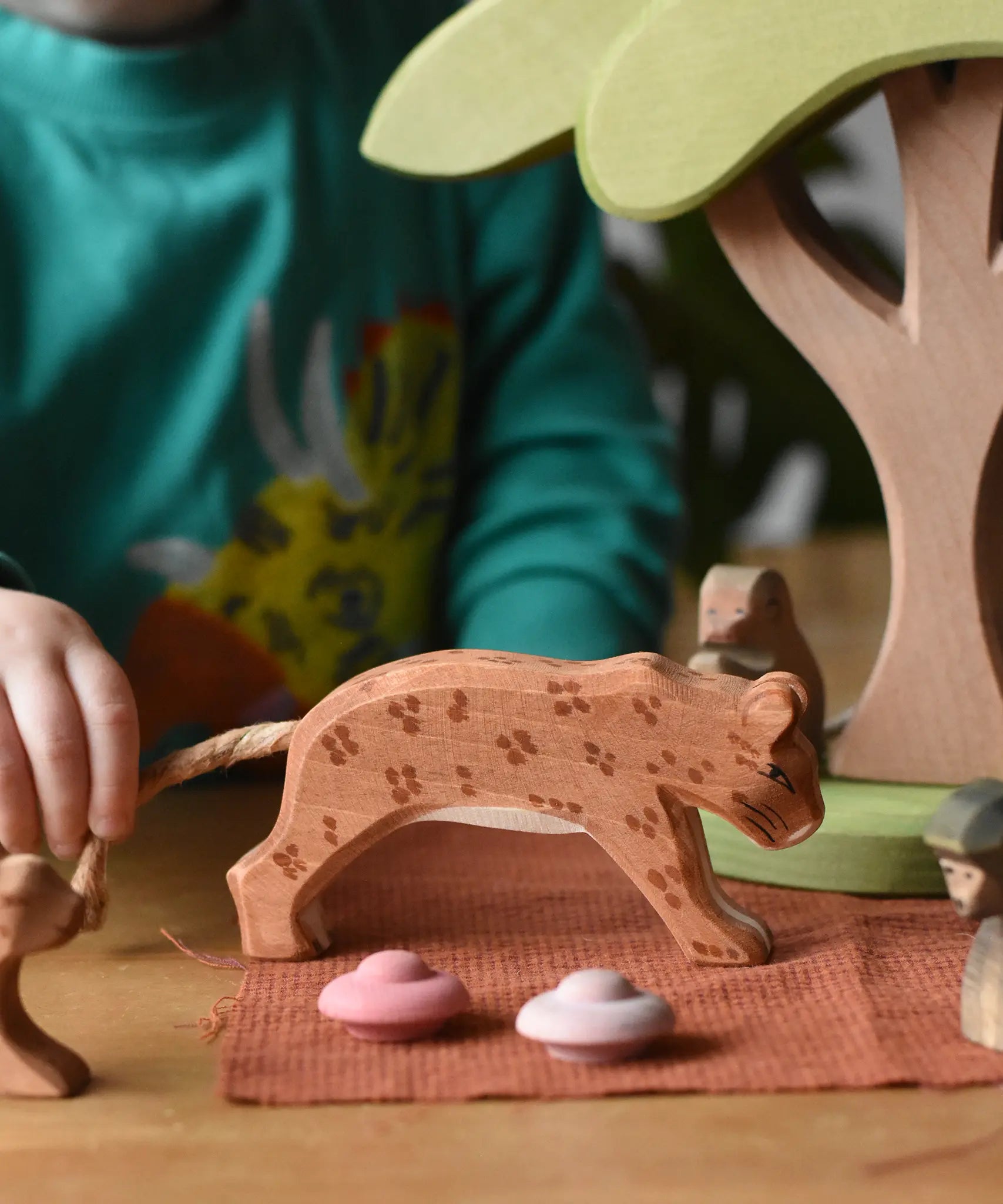 Ostheimer leopard placed in a small world play scene with a child holding it's rope tail.