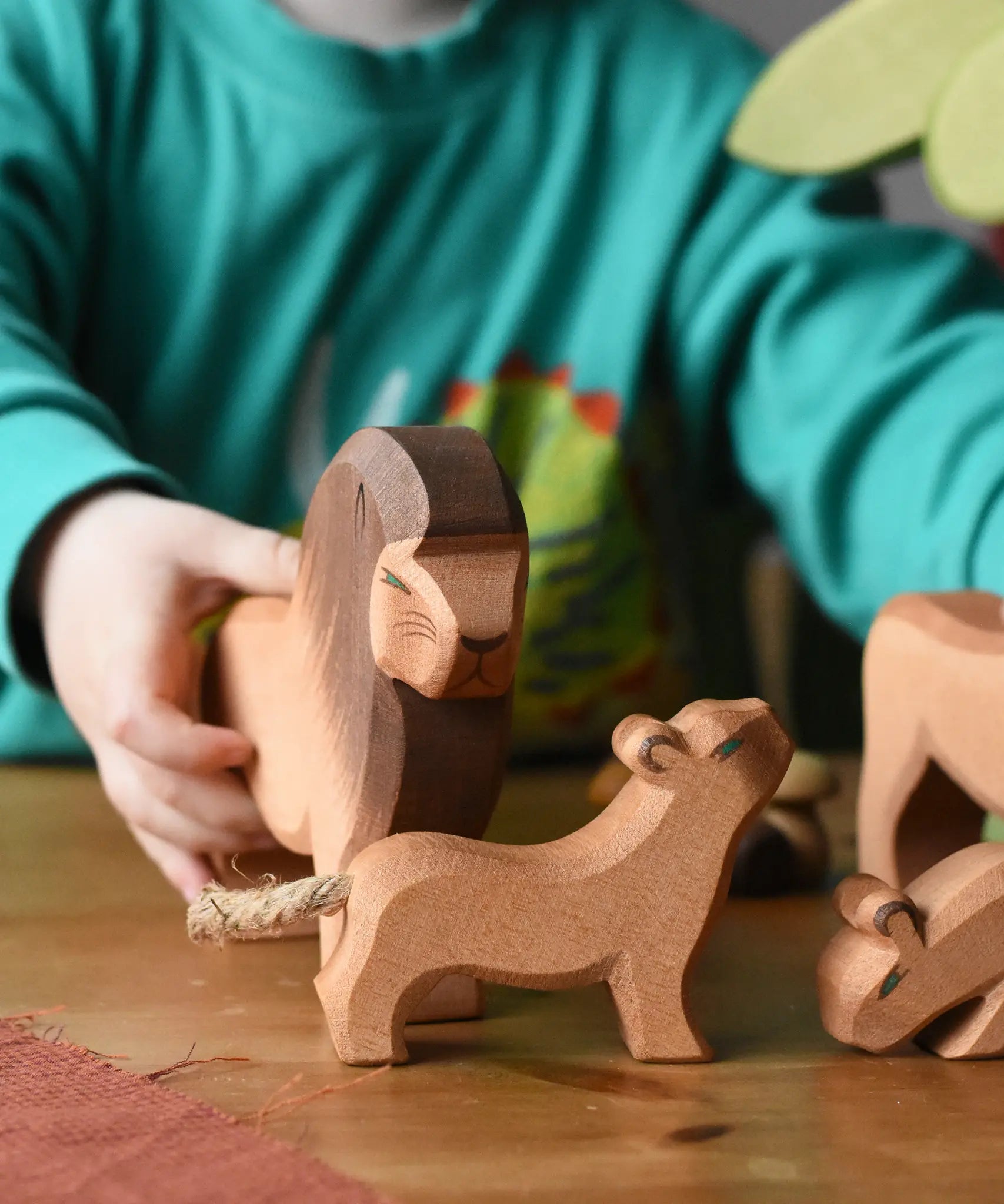 Ostheimer small lion cub with head high wooden toy figure placed on a wooden surface with a lion behind. 