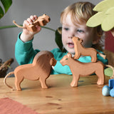 Child playing with Ostheimer lion family wooden toy figures in a small world play scene. 