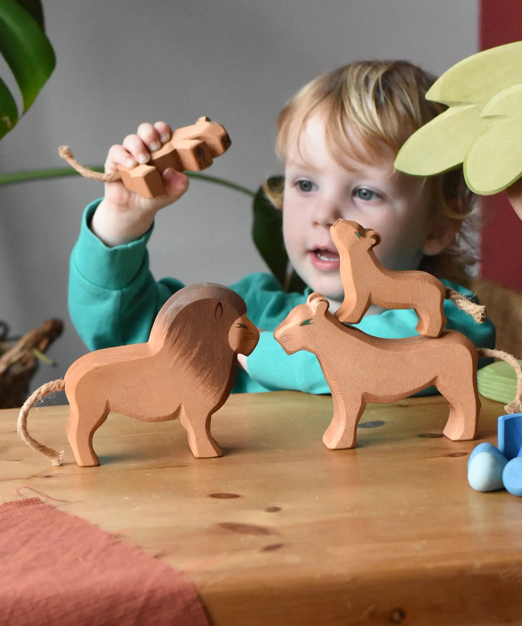 Child playing with Ostheimer lion family wooden toy figures in a small world play scene. 