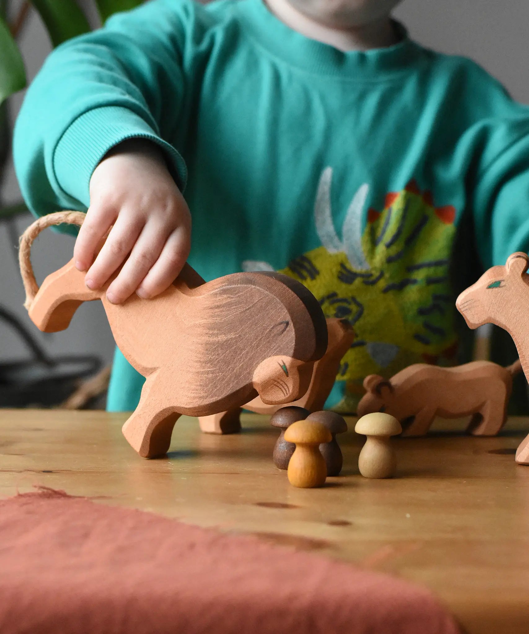 Child holding the Ostheimer male lion wooden toy figure tilting it forwards towards Grapat brown mushroom mandala pieces. 
