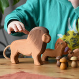 Ostheimer male lion wooden toy figure placed in a small world play set up with Grapat mandala mushrooms. A child's hand is reaching the for the lion.
