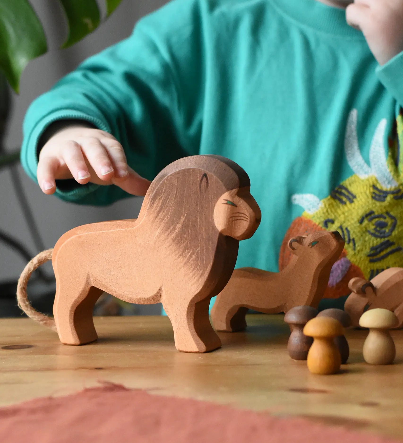 Ostheimer male lion wooden toy figure placed in a small world play set up with Grapat mandala mushrooms. A child's hand is reaching the for the lion.