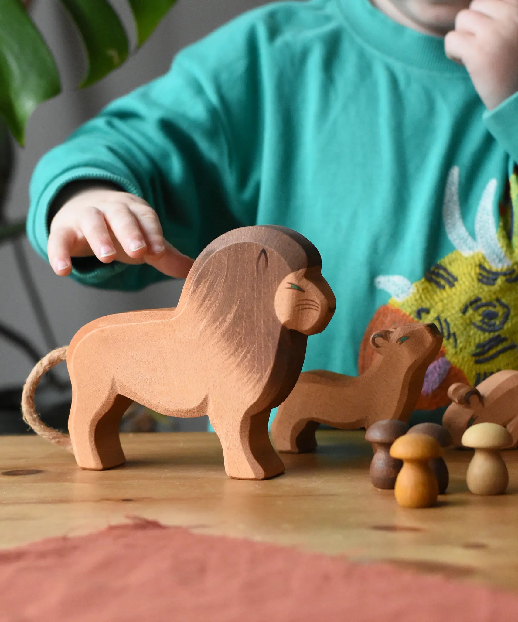 Ostheimer male lion wooden toy figure placed in a small world play set up with Grapat mandala mushrooms. A child's hand is reaching the for the lion.