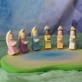 A host of little Ostheimer angels placed on a pond scene piece in a small world play set up. These little angel figures all have different coloured dresses, white, yellow, orange, purple, pink and blue with moon shaped wings. These wooden figures are part of a wide range of expertly hand crafted wooden toys here at Babipur. 