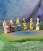 A host of little Ostheimer angels placed on a pond scene piece in a small world play set up. These little angel figures all have different coloured dresses, white, yellow, orange, purple, pink and blue with moon shaped wings. These wooden figures are part of a wide range of expertly hand crafted wooden toys here at Babipur. 