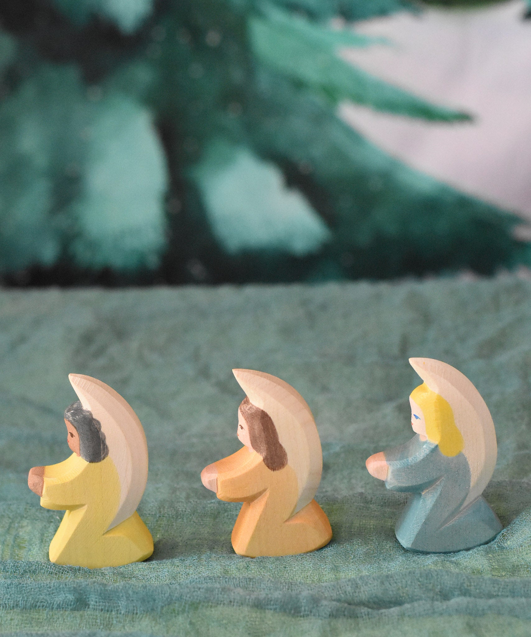 A group of three Ostheimer little angel figures placed on a green decorative cloth. There is a yellow, orange and blue coloured angel. These wooden figures are part of a wide range of expertly hand crafted wooden toys here at Babipur. 