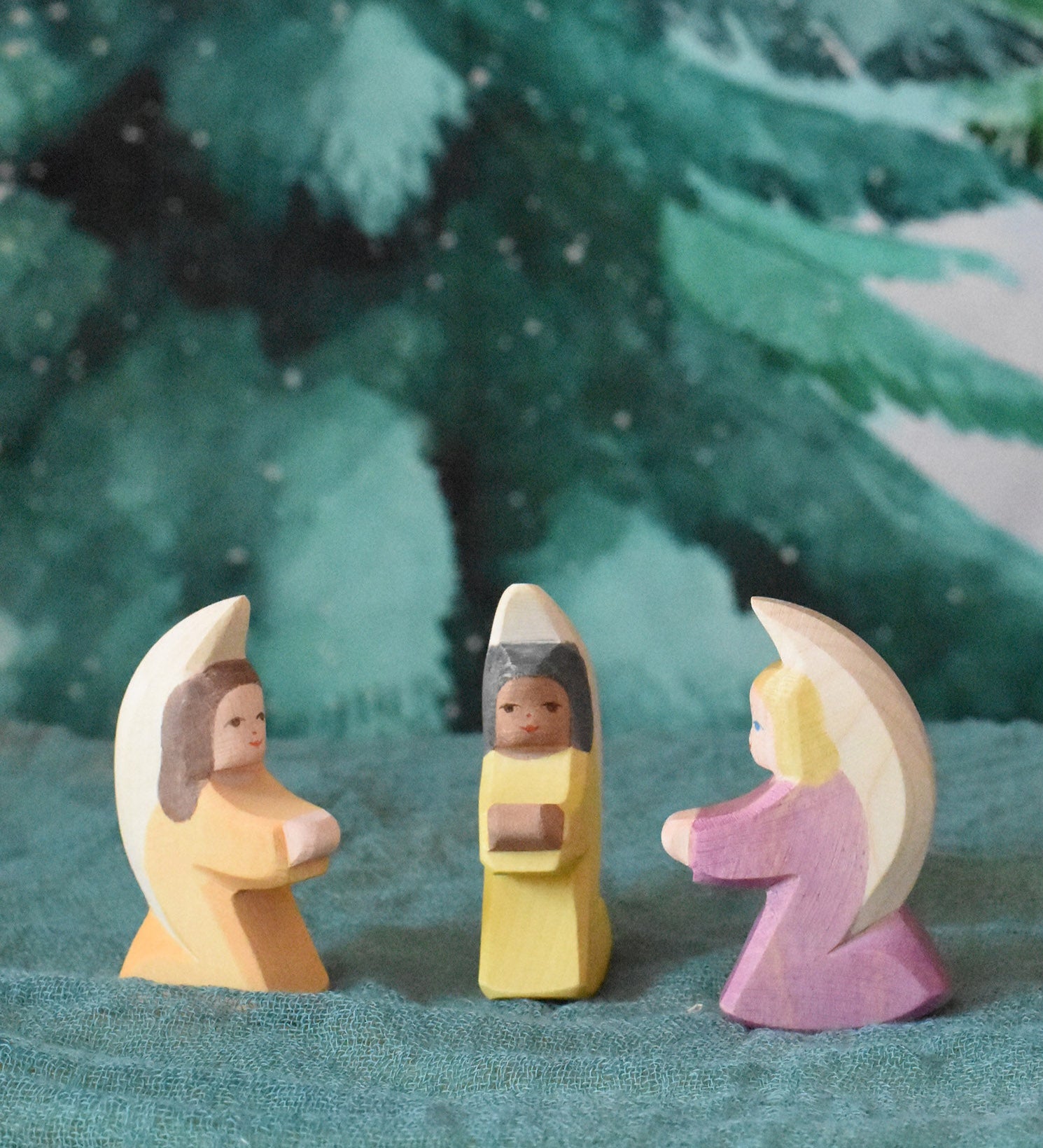 A group of three little wooden angels placed on an Ostheimer pond piece in a small world scene set up. These wooden figures are part of a wide range of expertly hand crafted wooden toys here at Babipur. 