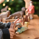 A close up of a child's hand reaching for an Ostheimer lying shepherd wooden toy figure. These wooden figures are part of a wide range of expertly hand crafted wooden toys here at Babipur. 
