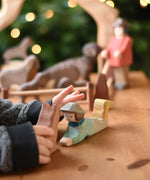 A close up of a child's hand reaching for an Ostheimer lying shepherd wooden toy figure. These wooden figures are part of a wide range of expertly hand crafted wooden toys here at Babipur. 