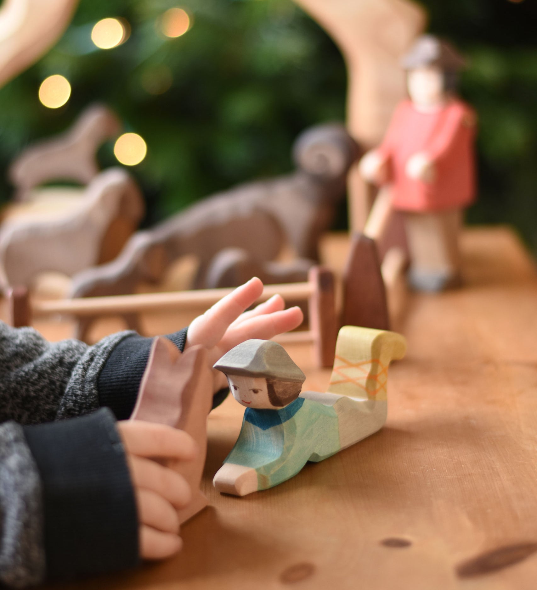 A close up of a child's hand reaching for an Ostheimer lying shepherd wooden toy figure. These wooden figures are part of a wide range of expertly hand crafted wooden toys here at Babipur. 