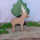 An Ostheimer male deer toy figure placed in the middle of a small world play scene. Ostheimer grass an oak tree figure can be seen in the background. Check out our full range of expertly crafted wooden toy figures and scenery here at Babipur.