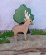 An Ostheimer male deer toy figure placed in the middle of a small world play scene. Ostheimer grass an oak tree figure can be seen in the background. Check out our full range of expertly crafted wooden toy figures and scenery here at Babipur.
