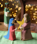 Ostheimer Mary and Joseph wooden toy figures in a festive small world play scene with fairy lights in the background.