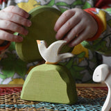 Ostheimer white dove bird figure placed on a middle green bush on a rattan top stool placed in a simple small world play scene. 