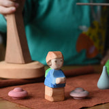 Ostheimer Mo handmade little boy wooden toy figure placed on a brown cloth with pink Grapat mandala pieces around it.