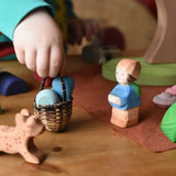 Ostheimer Mo handmade wooden toy figure placed in a small world play scene with a small kraul basket filled with a few Grapat mandala pieces.