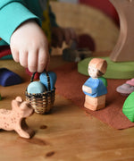 Ostheimer Mo handmade wooden toy figure placed in a small world play scene with a small kraul basket filled with a few Grapat mandala pieces.