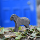 An Ostheimer wooden Moorland lamb figure placed on a stone wall outdoors. These wooden figures are part of a large range of expertly hand crafted, Waldorf inspired, wooden toys here at Babipur.
