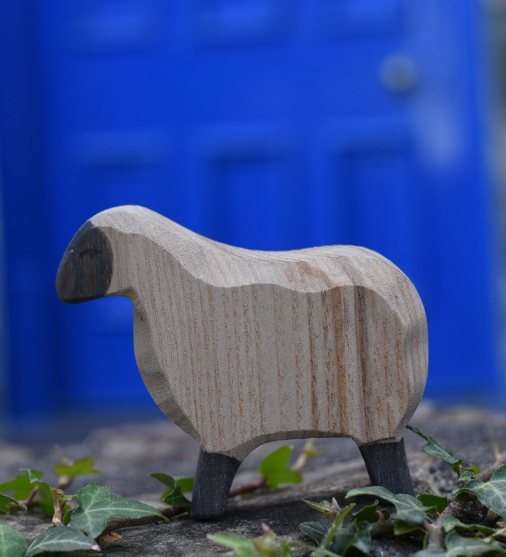 An Ostheimer moorland sheep placed on a stone wall outdoors. These wooden figures are part of a large range of expertly hand crafted, Waldorf inspired, wooden toys here at Babipur.
